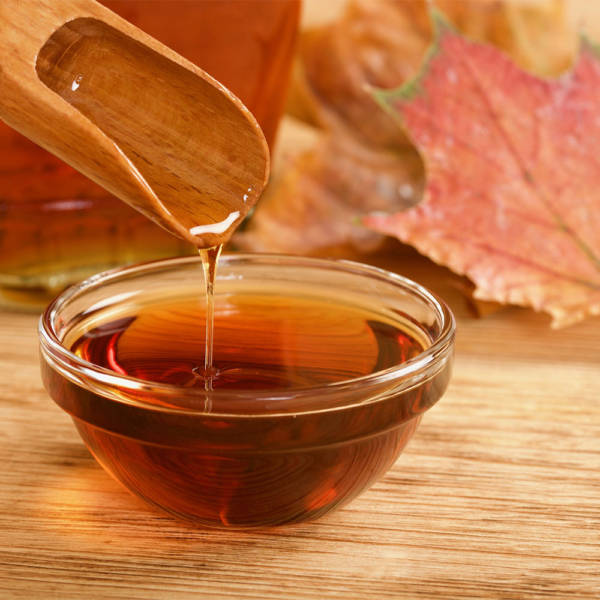 organic maple syrup pouring from wood spoon into glass dish, with leaves behind